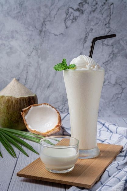 a drink with whipped cream and coconut on a cutting board next to two pieces of fruit