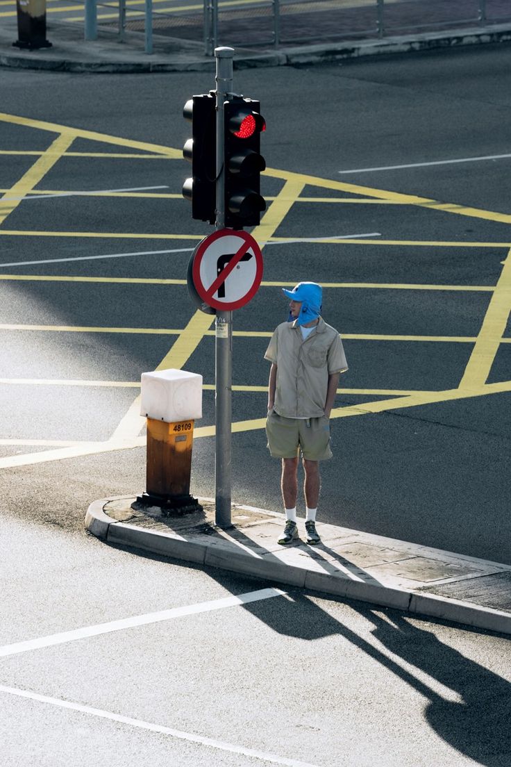 a man standing next to a traffic light with a blue hat on his head and no left turn sign in the foreground