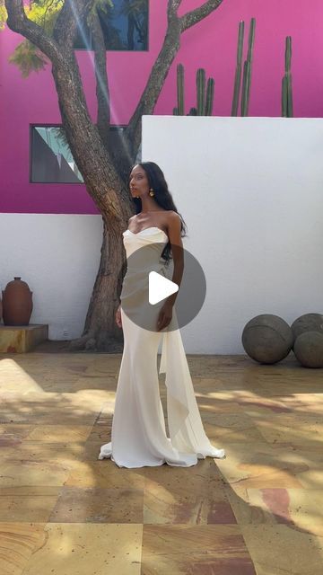 a woman in a white dress standing next to a tree