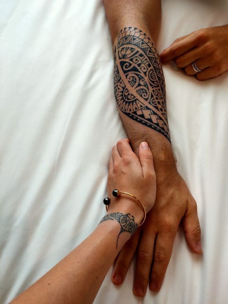 two people holding hands on top of a white bed covered in sheets with tattoos on their arms