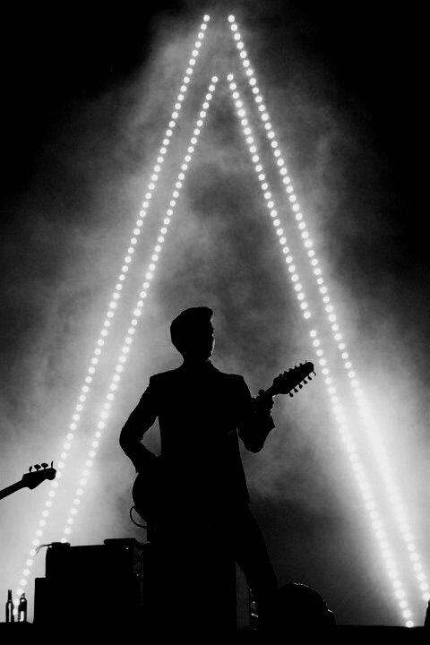 a man standing in front of a guitar on top of a stage with lights behind him