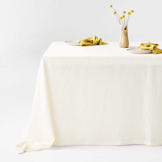 a white table topped with two plates covered in yellow napkins next to a vase filled with flowers