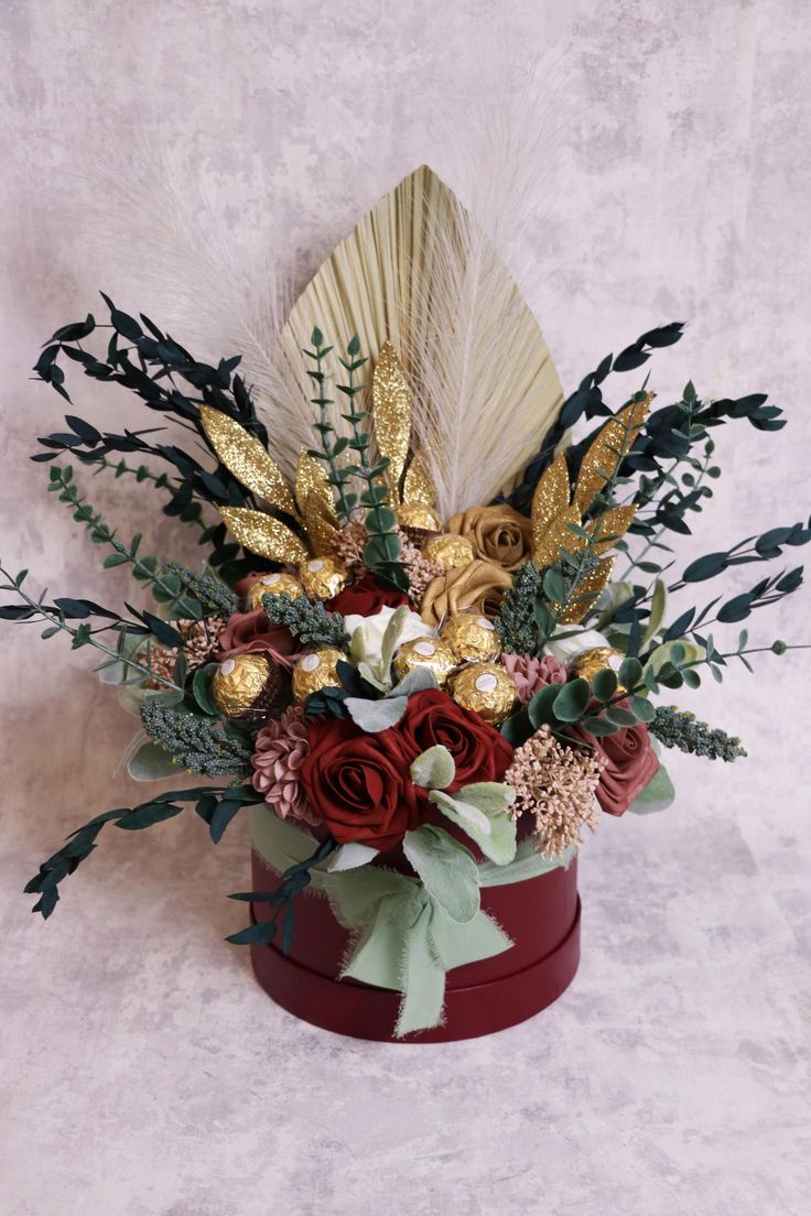 an arrangement of flowers and feathers in a red box on a white background with gold accents