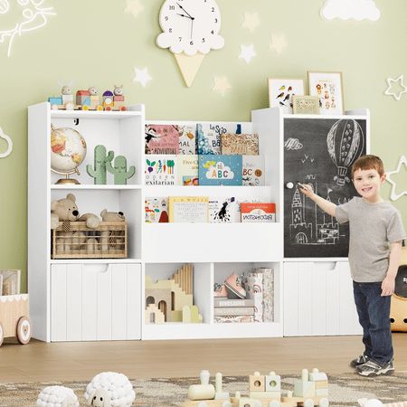 a young boy standing in front of a white bookcase filled with books and toys