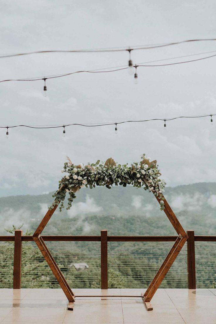 a wooden arch decorated with flowers and greenery on top of a building overlooking the mountains