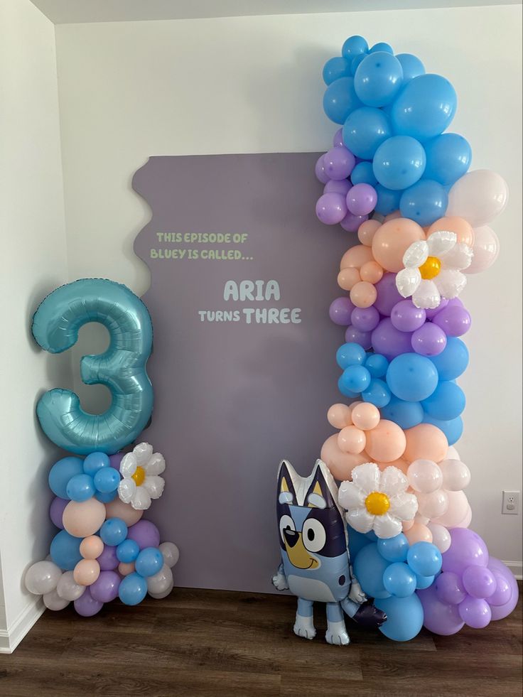 the balloon arch is decorated with blue, pink and white balloons that spell out three