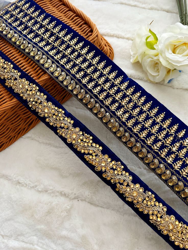 two pieces of blue and gold thread work on a white surface with flowers in the background