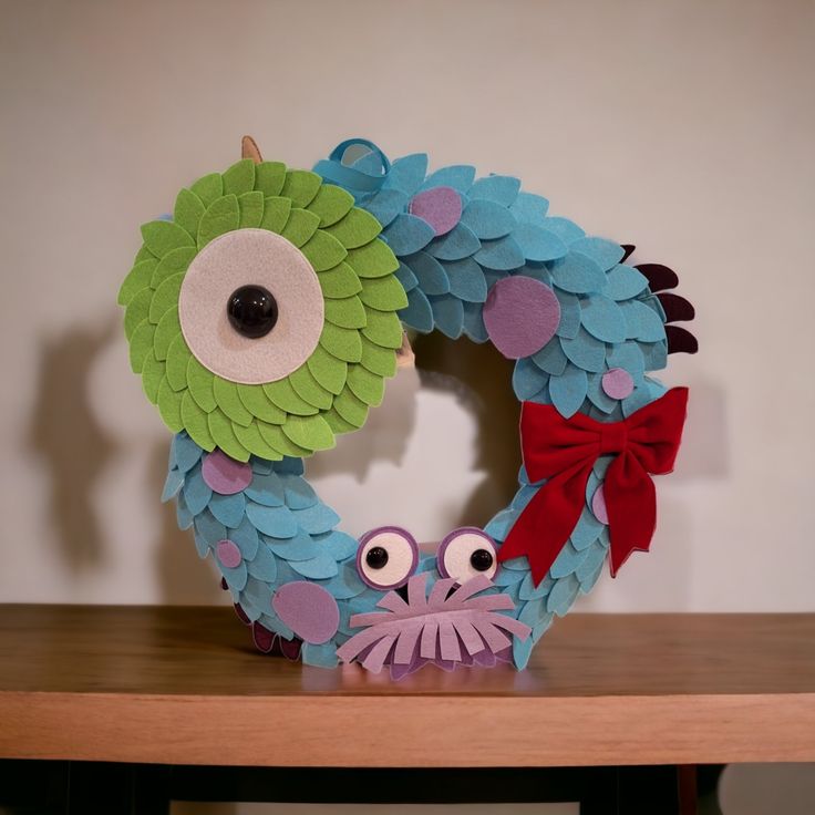 a paper wreath with two eyes and a red bow on top of a wooden table