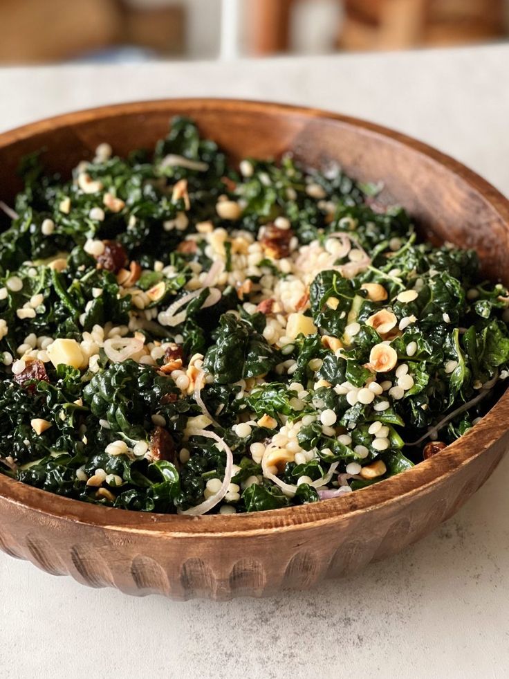 a wooden bowl filled with spinach and other food on top of a white table