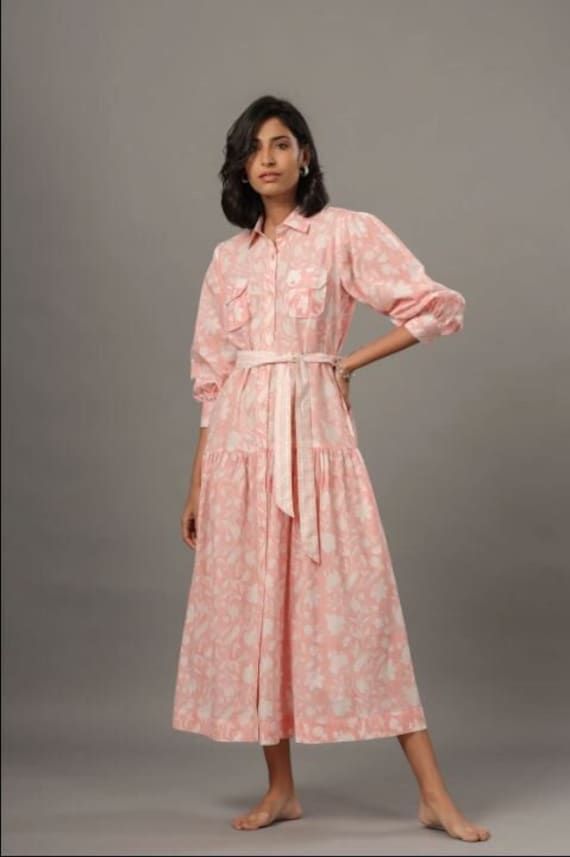 Made of breathable cotton, this pink shirt dress is a perfect spring/summer look. Beautifully hand block printed, with subtle ruffle details and a removable belt completes this feminine look. Delicate Hand wash Belted Cotton Shirt Dress For Spring, Spring Cotton Belted Shirt Dress, Cotton Belted Shirt Dress For Spring, Feminine Spring Cotton Shirt Dress, Feminine Cotton Shirt Dress For Spring, Pink Cotton Shirt Dress For Summer, Long Sleeve Pink Cotton Shirt Dress, Pink Long Sleeve Cotton Shirt Dress, Summer Cotton Shirt Dress With Ruffles