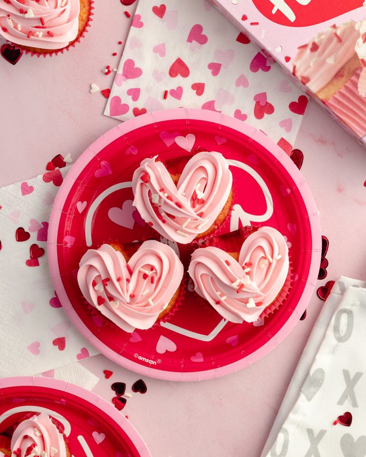 cupcakes with pink frosting in the shape of hearts on red plates next to valentine's day napkins