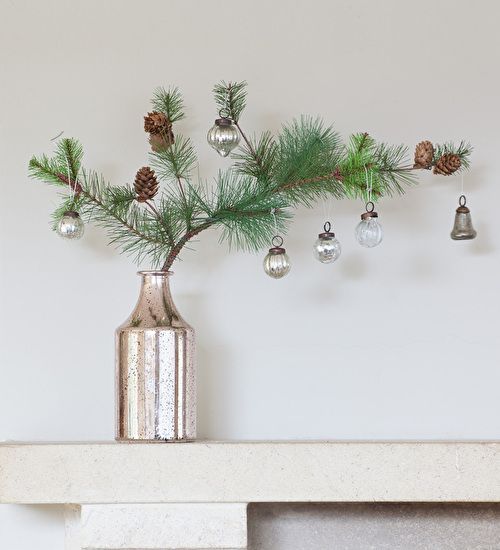 a silver vase with pine cones and ornaments hanging from it's side on a shelf