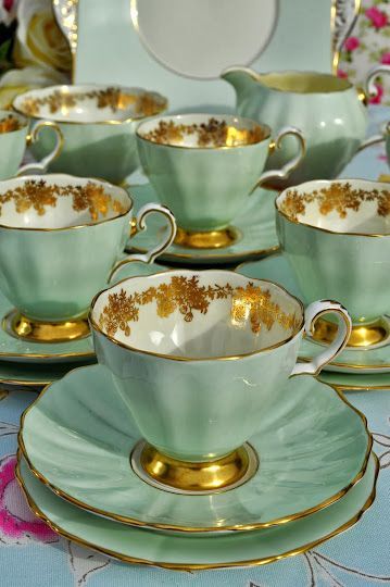 tea cups and saucers are sitting on a blue tablecloth with gold trimmings