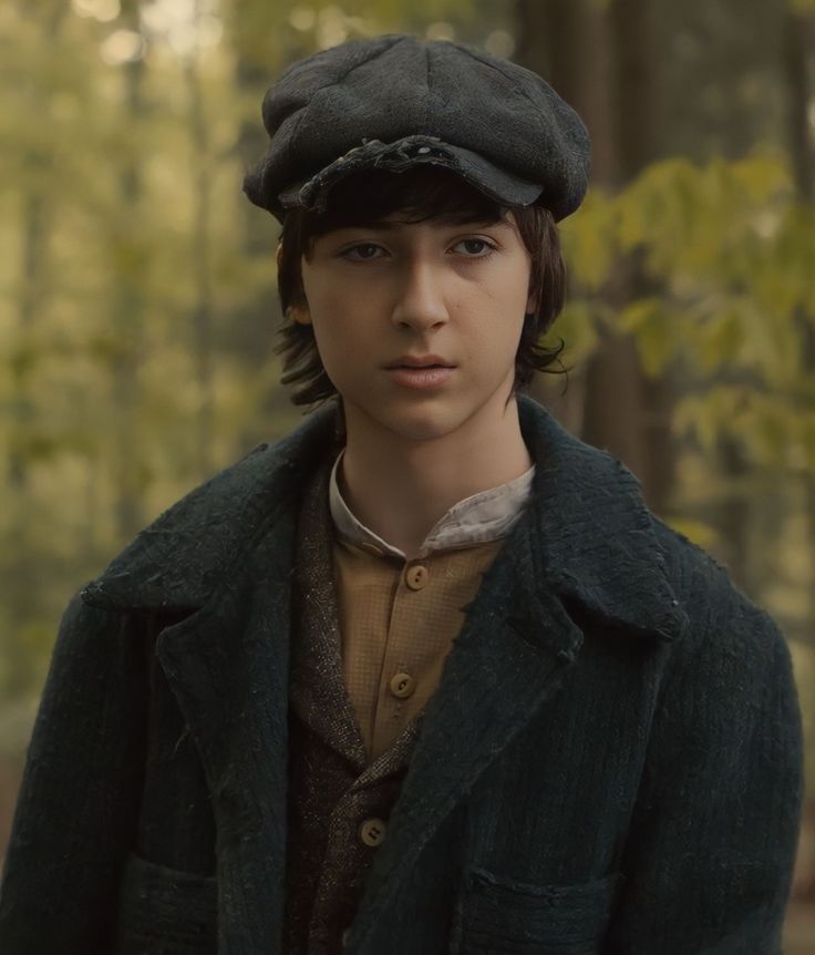 a young man wearing a hat and coat in the woods