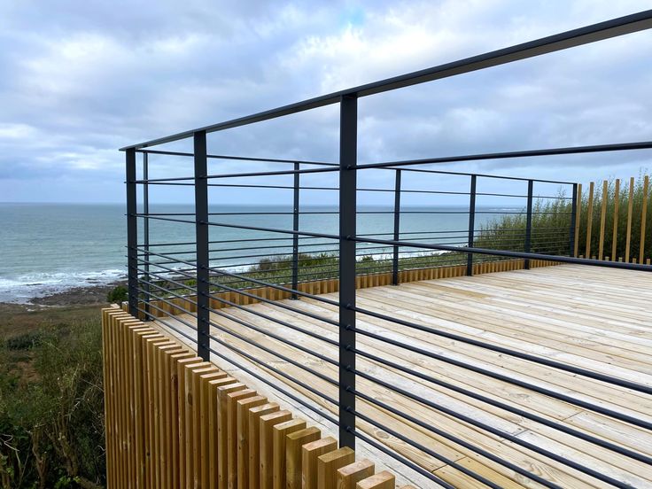 a wooden deck next to the ocean with railings on each side and water in the background