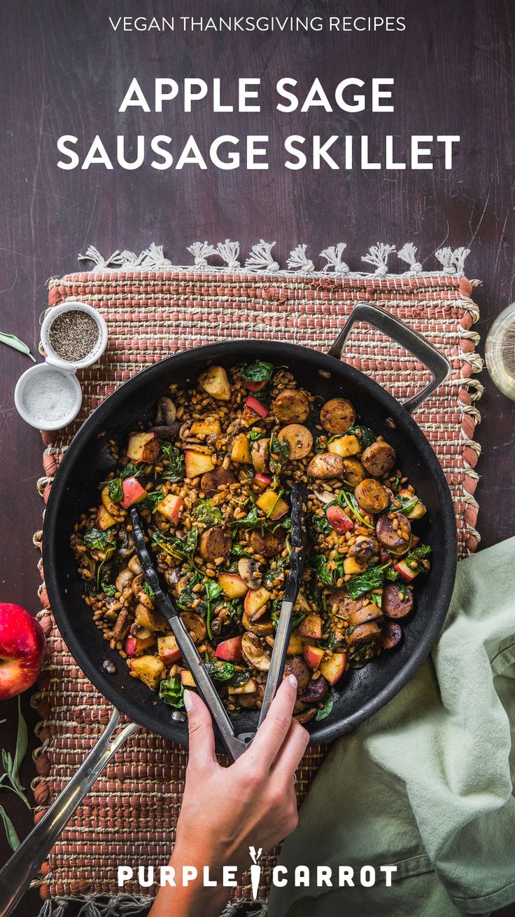 a skillet filled with sausage and vegetables on top of a table next to apples