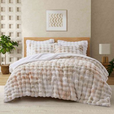 a bed with white and brown comforters in a room next to a potted plant