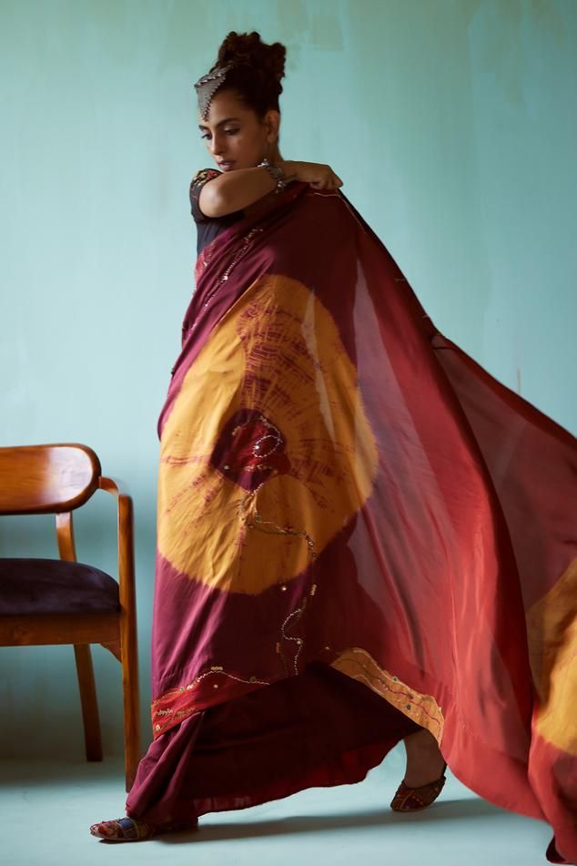 Maroon and mustard habutai silk saree with tie-dye pattern and mirror and thread hand embroidery. Comes with a black handwoven chiniya silk blouse.
Components: 2
Pattern: Hand embroidered
Type Of Work: Tie-Dye, Mirror, Thread
Neckline: V Neck
Sleeve Type: Half
Fabric: Saree: Habutai silk, Blouse: Handwoven chiniya silk
Color: Maroon
Other Details: 
Note: Head accessory worn by the model is not for sale.
Occasion: Wedding - Aza Fashions Bohemian Silk Pre-draped Saree For Puja, Festival Cotton Silk Saree With Batik Print, Cotton Silk Saree With Batik Print For Festivals, Festive Chanderi Blouse Piece With Batik Print, Chanderi Saree With Batik Print, Chanderi Saree With Batik Print For Navratri, Chanderi Batik Print Blouse Piece For Festivals, Festive Batik Print Art Silk Saree, Festive Chanderi Saree With Batik Print