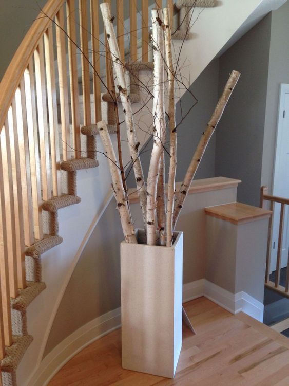 a tall vase filled with branches sitting on top of a wooden floor next to a stair case