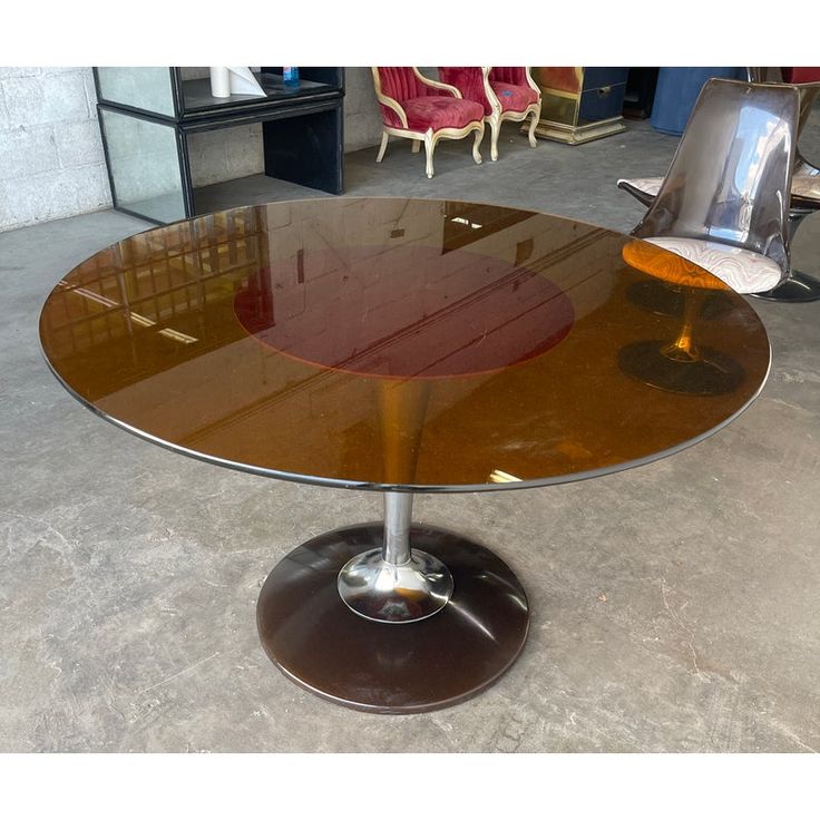 an oval glass table with metal base in a room filled with chairs and other furniture