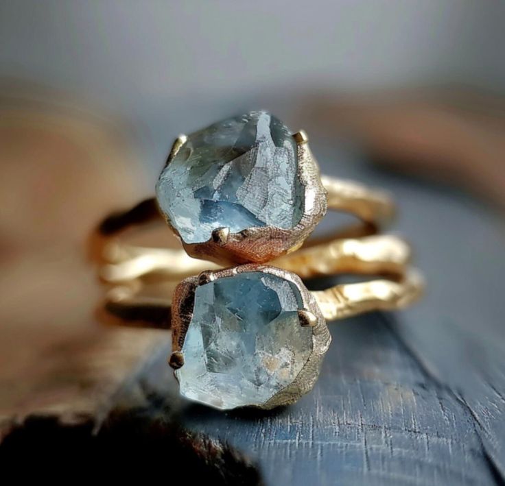 two gold rings with blue topazte stones on each one, sitting on a piece of wood