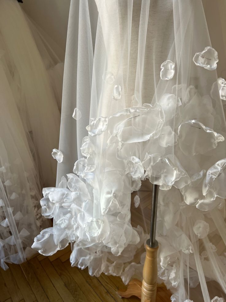 the dress is being displayed on a mannequin with sheer white fabric and flowers