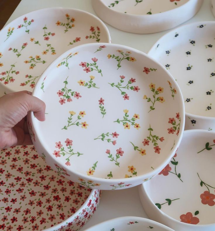 a person is holding a bowl in front of many plates that have flowers on them