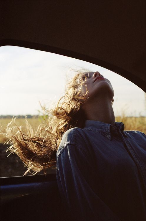 a woman laying down in the back seat of a car with her hair blowing in the wind