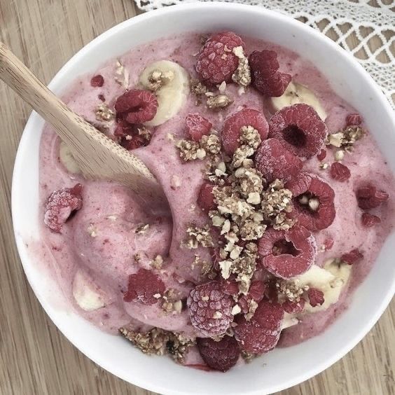 a bowl of ice cream with raspberries and walnuts in it next to a lace doily