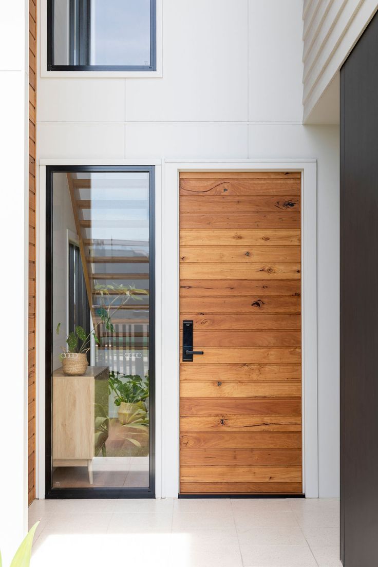 a wooden door in front of a white wall and floor with plants on the side