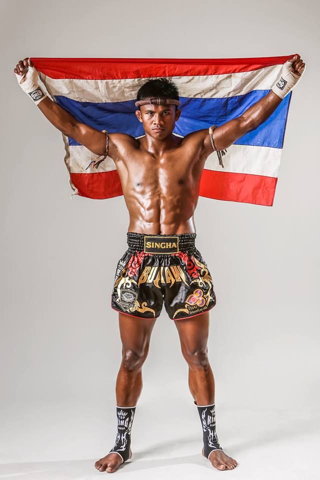 a shirtless man holding a flag in front of his face and chest, with one arm raised