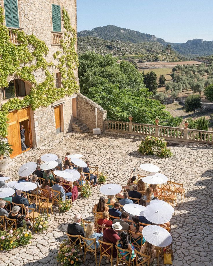 several people sitting at tables under umbrellas in front of an old building with stone floors