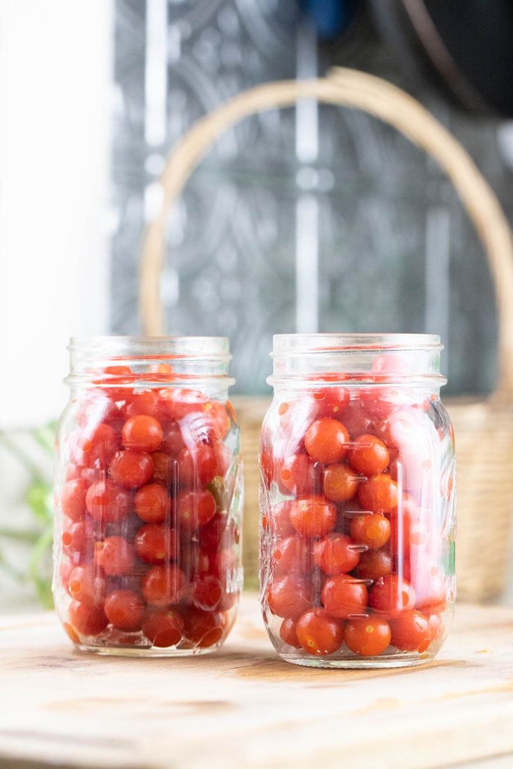 two jars filled with tomatoes sitting on top of a wooden table