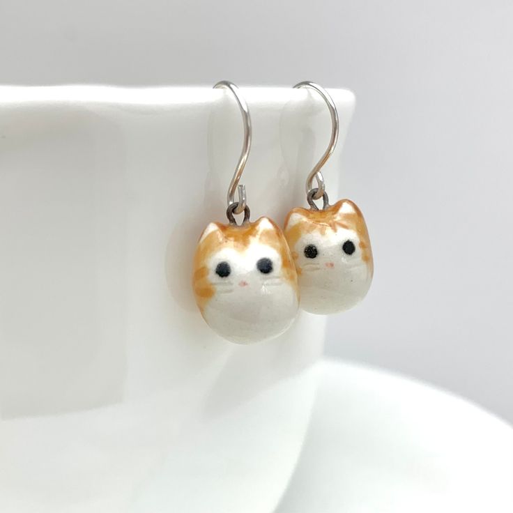 "Product Information Cute and round orange tabbies for any outfit or occasion! Available with Sterling Silver or Gold-Filled ear wires. *I can also make you an all orange tabby cat pair by request. Dimensions Each earring charm is about 3/8\" (0.9 cm) - 1/2\" (1.3 cm) tall. Materials Porcelain Clay Underglaze Colors Mid-Fire Clear Glaze Sterling Silver / Gold-Filled Ear Wires Care Instructions While porcelain clay is durable, it is not shatter-proof. Please wear and handle with care!  Earrings m Clay Underglaze, Earrings Ceramic, Orange Tabby Cats, Orange Tabby, Porcelain Clay, Cat Jewelry, Cat Lover Gift, Gift Cute, Cat Earrings