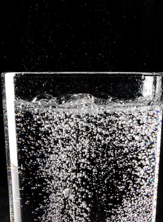 a glass filled with water sitting on top of a table next to a black background