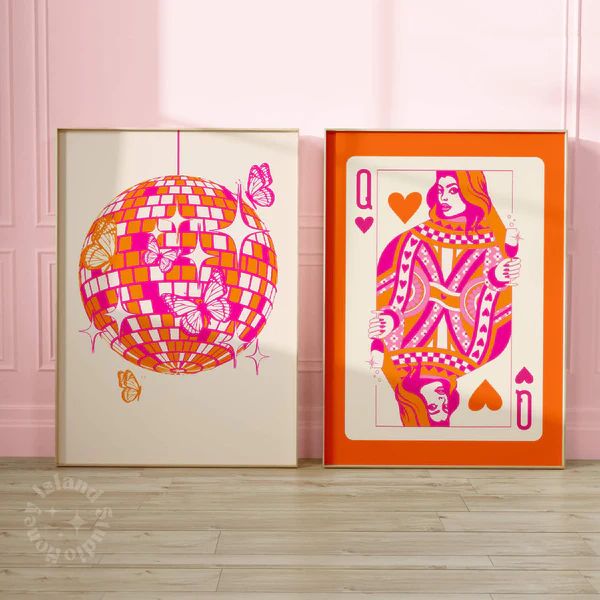 two colorful playing cards sitting next to each other on a wooden floor in front of a pink wall