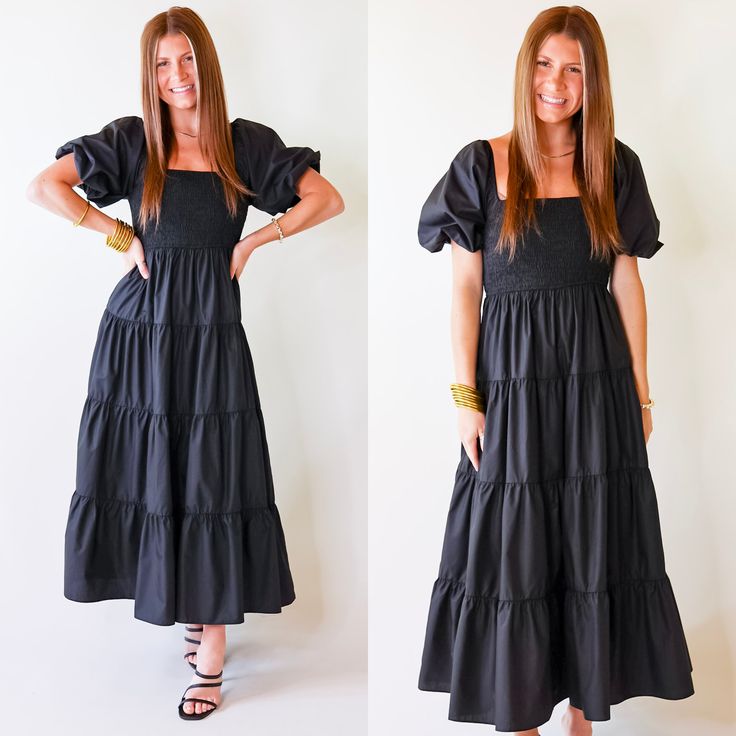 Model is wearing a long black dress featuring puffed balloon sleeves, smocked bodice, and tiered skirt. Tiered Midi Dress With Gathered Sleeves, Black Tiered Skirt Dress With Ruched Detail, Black Ruched Dress With Tiered Skirt, Black Midi Dress With Gathered Sleeves For Brunch, Black Smocked Dress With Puff Sleeves, Black Tiered Skirt Dress For Brunch, Black Tiered Ruched Dress, Black Puff Sleeve Dress With Ruffle Hem, Black Ruched Tiered Dress