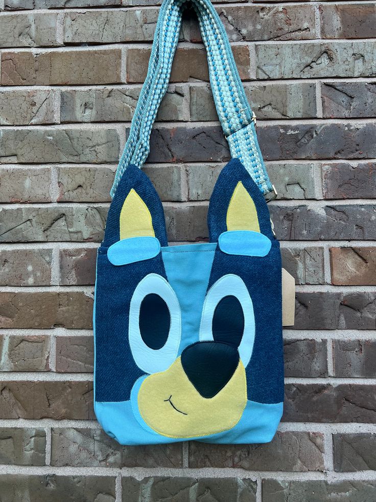 a blue and yellow bag with a dog face on it hanging from a brick wall