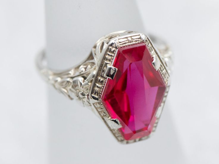 This fantastic Art Deco era ring is iconic of the early 1900s, with a perfectly preserved synthetic ruby gemstone set at its center. In the Victorian era, transportation was far more expensive than it is now. Rubies had to be brought from Burma, and Emeralds from South America. This cost translated into the price of the stones, making them far too expensive for the average consumer. In response, jewelers found interesting ways to make natural stones go a little farther. Synthetics were created: stones faceted from crystals grown in laboratories. These remained popular right through the Art Deco era. Metal: 18K White GoldGem: Synthetic Ruby Gem Measurements: 12.0 x 8.1 mm, Fancy CutRing Size: 4Marks: “18” Stamped on the inside band Red Engraved Signet Ring For Formal Occasion, Formal Red Engraved Signet Ring, Formal Octagon Ruby Jewelry, Heirloom Ruby Signet Ring With Hallmark, Red Art Deco Jewelry For Formal Occasions, Red Art Deco Hallmarked Jewelry, Vintage Rings With Octagon Center Stone, Vintage Silver Octagon Ring, Vintage Octagon Ring With Center Stone