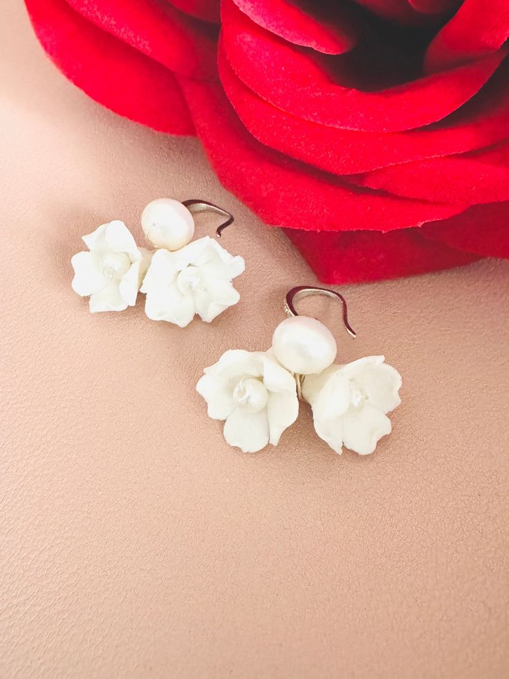 two white flowers are sitting next to a red rose on a pink surface with the petals still attached