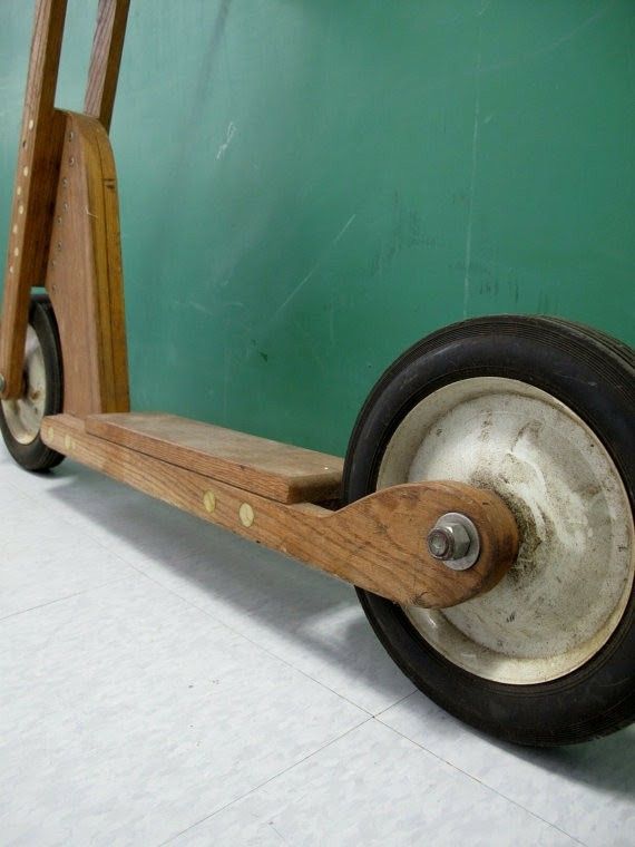 an old wooden scooter with two wheels on the front and back wheel, sitting against a green wall