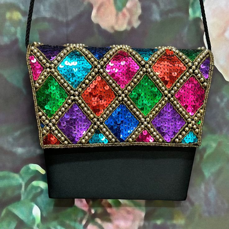 "Vintage 80's shoulder purse has bright rainbow sequins edged with gold beads in a harlequin pattern on the front flap. The body of the purse is black satin. It has a braided shoulder cord and magnetic snap front closure. The cord folds in to convert to a clutch. Interior is black satin with one pocket. Clean condition inside and out with a light mark on the back. Purse measures 7.5\" at its widest by 6.5\". Please see photos for more details. All items are vintage that are preowned. All of the Multicolor Sequined Evening Bag, Multicolor Sequined Shoulder Bag For Party, Evening Multicolor Sequins Bag, Multicolor Shoulder Bag For Party Festivals, Multicolor Shoulder Bag For Evening Festivals, Multicolor Evening Bags For Festivals, Multicolor Evening Shoulder Bag For Festivals, Evening Multicolor Shoulder Bag For Festivals, Formal Multicolor Embellished Shoulder Bag