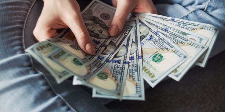 a person sitting on the floor with money in their lap and one hand reaching for it