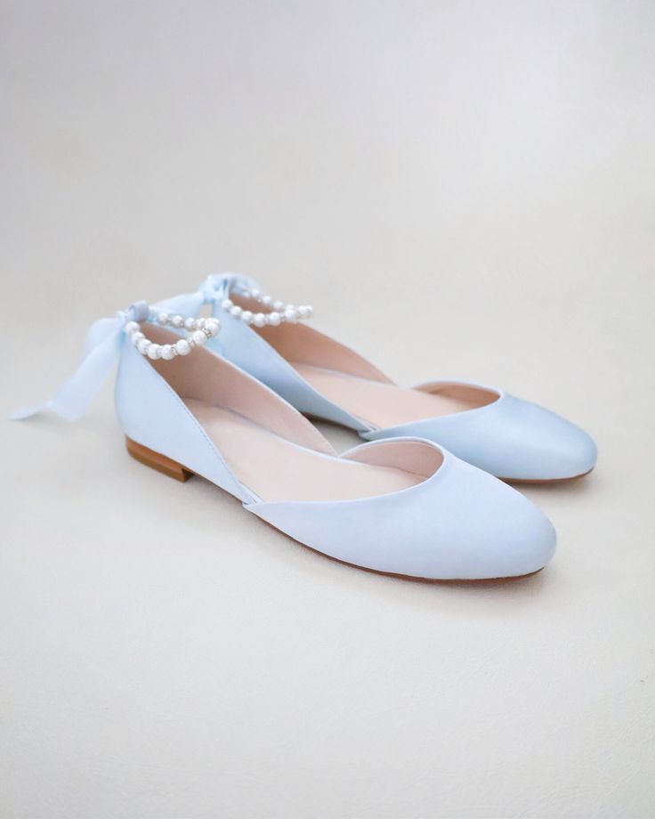 a pair of light blue shoes with pearls on the toe and heel, sitting on a white surface