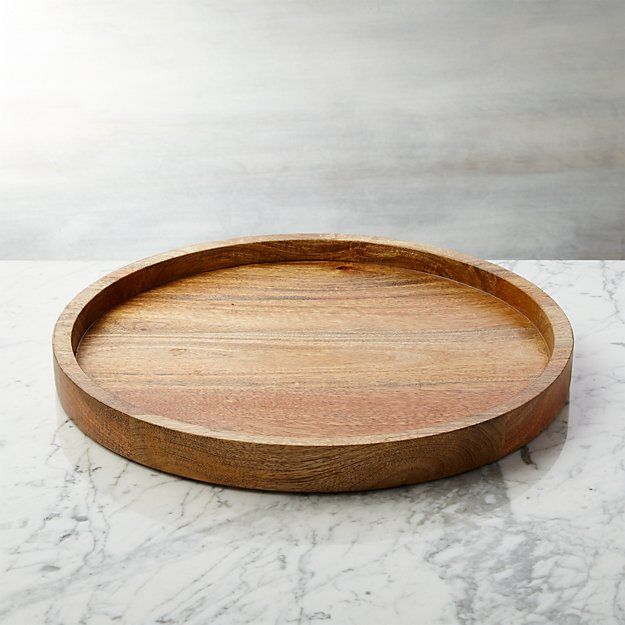 a round wooden tray sitting on top of a marble countertop next to a white wall