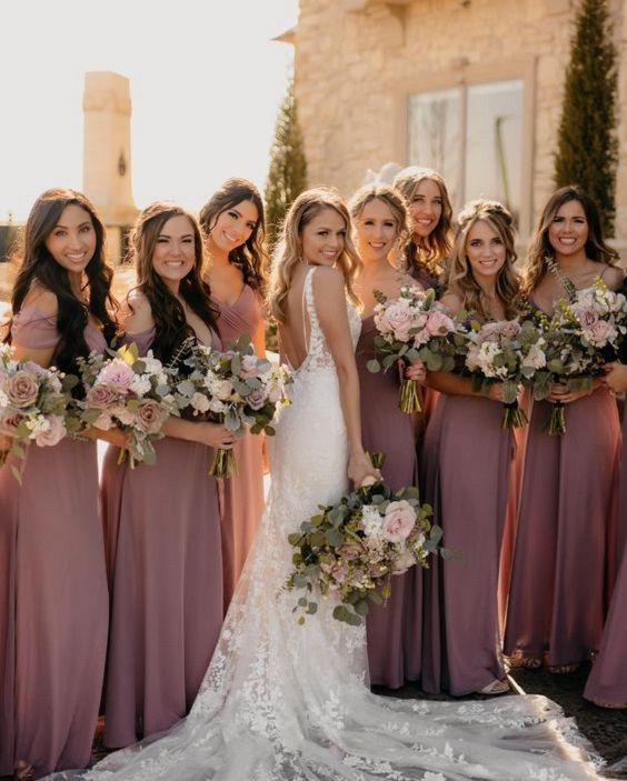 a group of women standing next to each other wearing dresses and holding bouquets in their hands