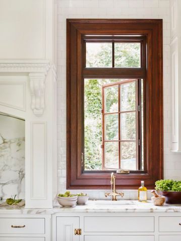 a kitchen with white cabinets and marble counter tops, an open window above the sink