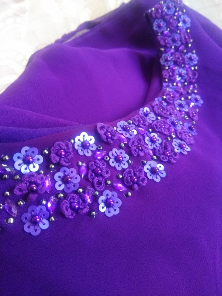 a purple dress with flowers on it and beads in the neckline is laying on a white surface