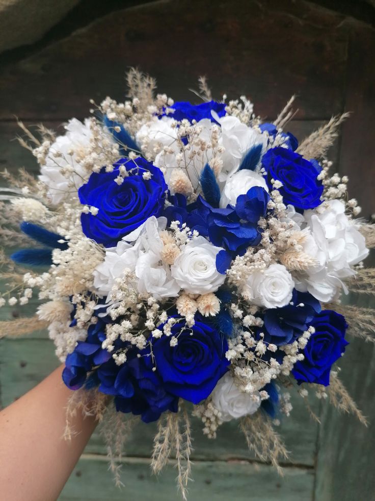 a bridal bouquet with blue and white flowers on it is being held by someone's hand