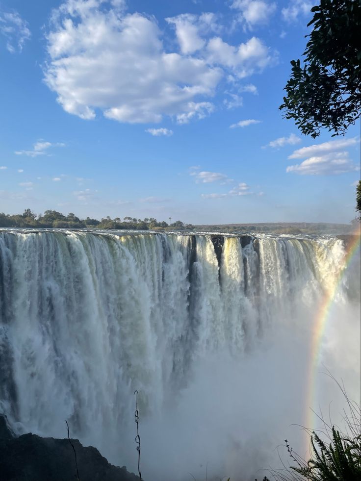 a rainbow shines in the sky above a large waterfall with water cascading it's sides